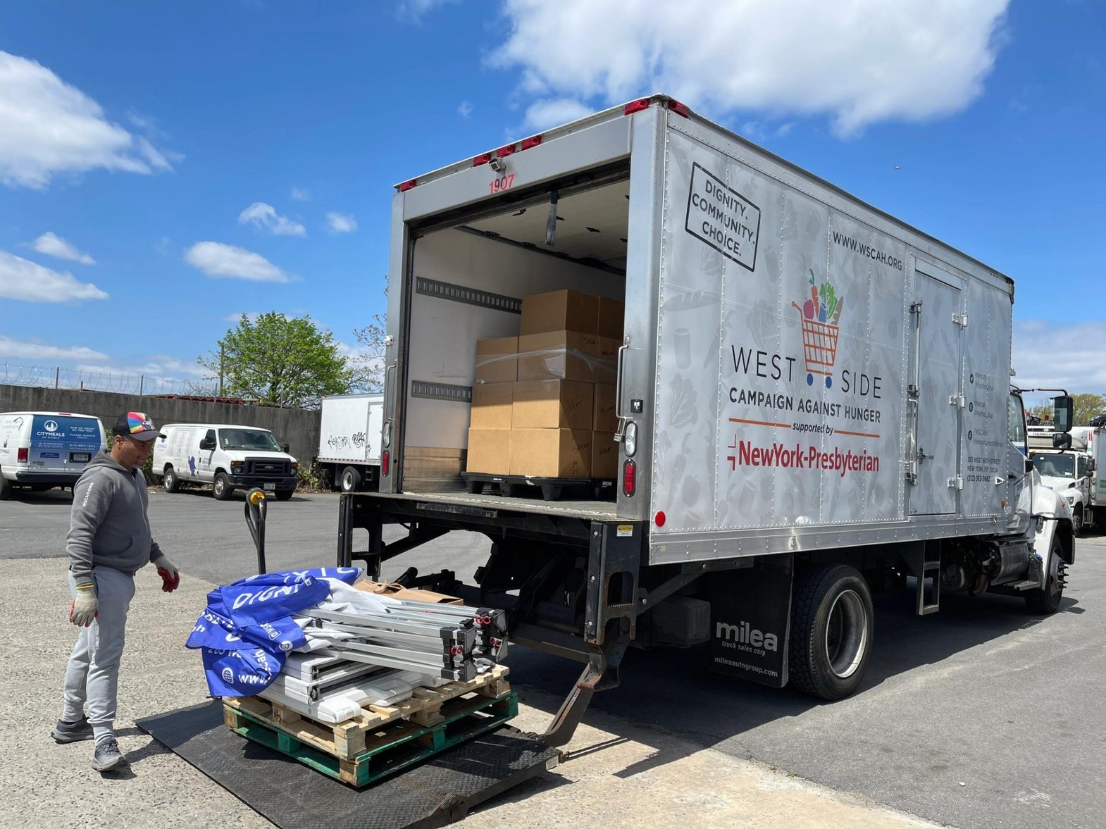 Under a blue sky, a WSCAH truck lifts deconstructed tents into its bed, preparing for a distribution.