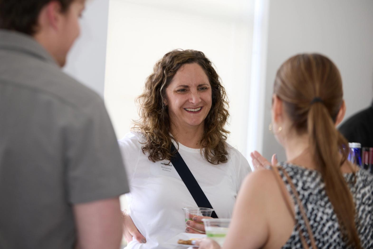 A woman holding a drink smiles while speaking with two others