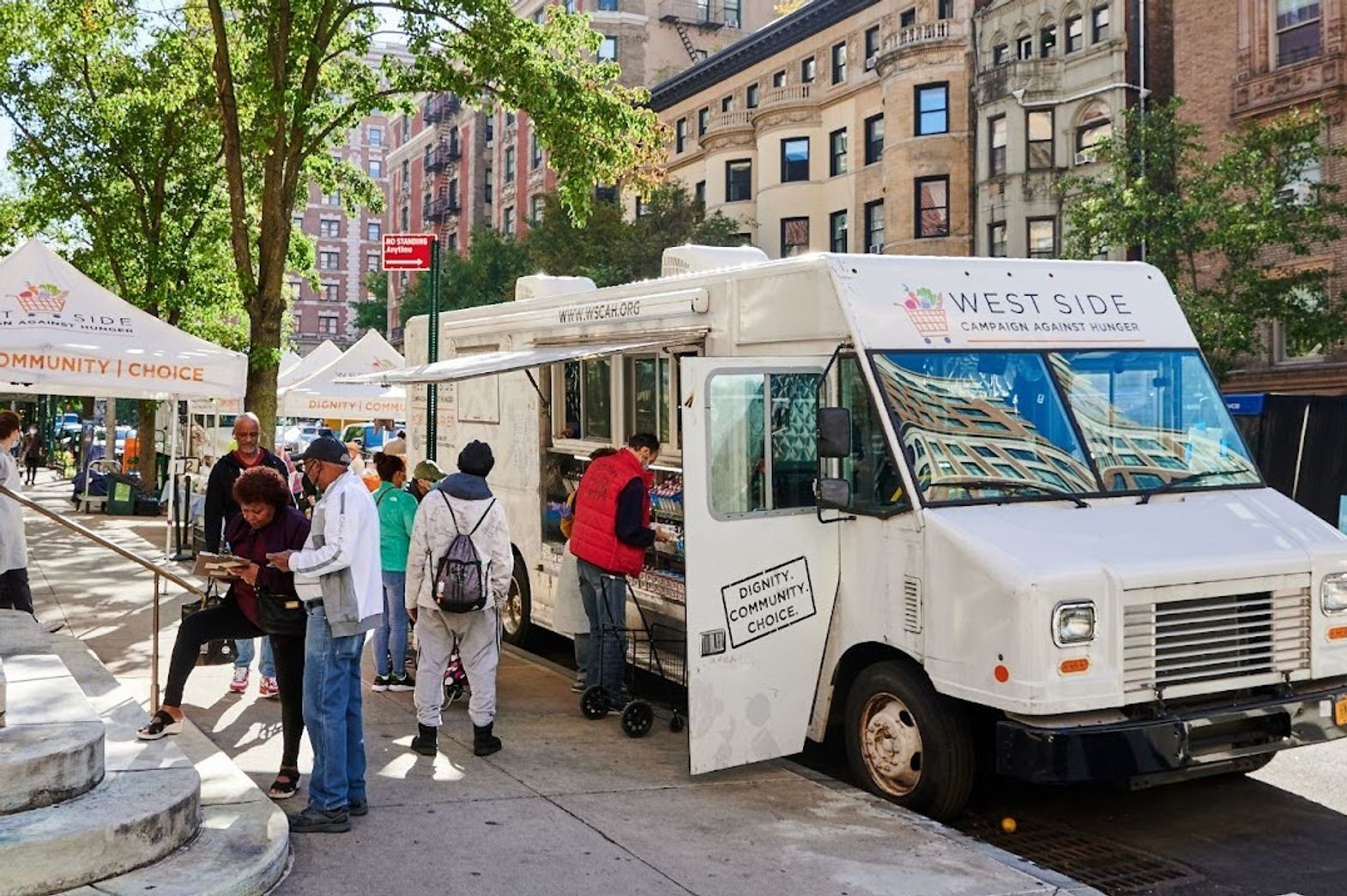 The sun shines on a WSCAH distribution at our 86th street location. Customers go up to WSCAH's van to receive food.