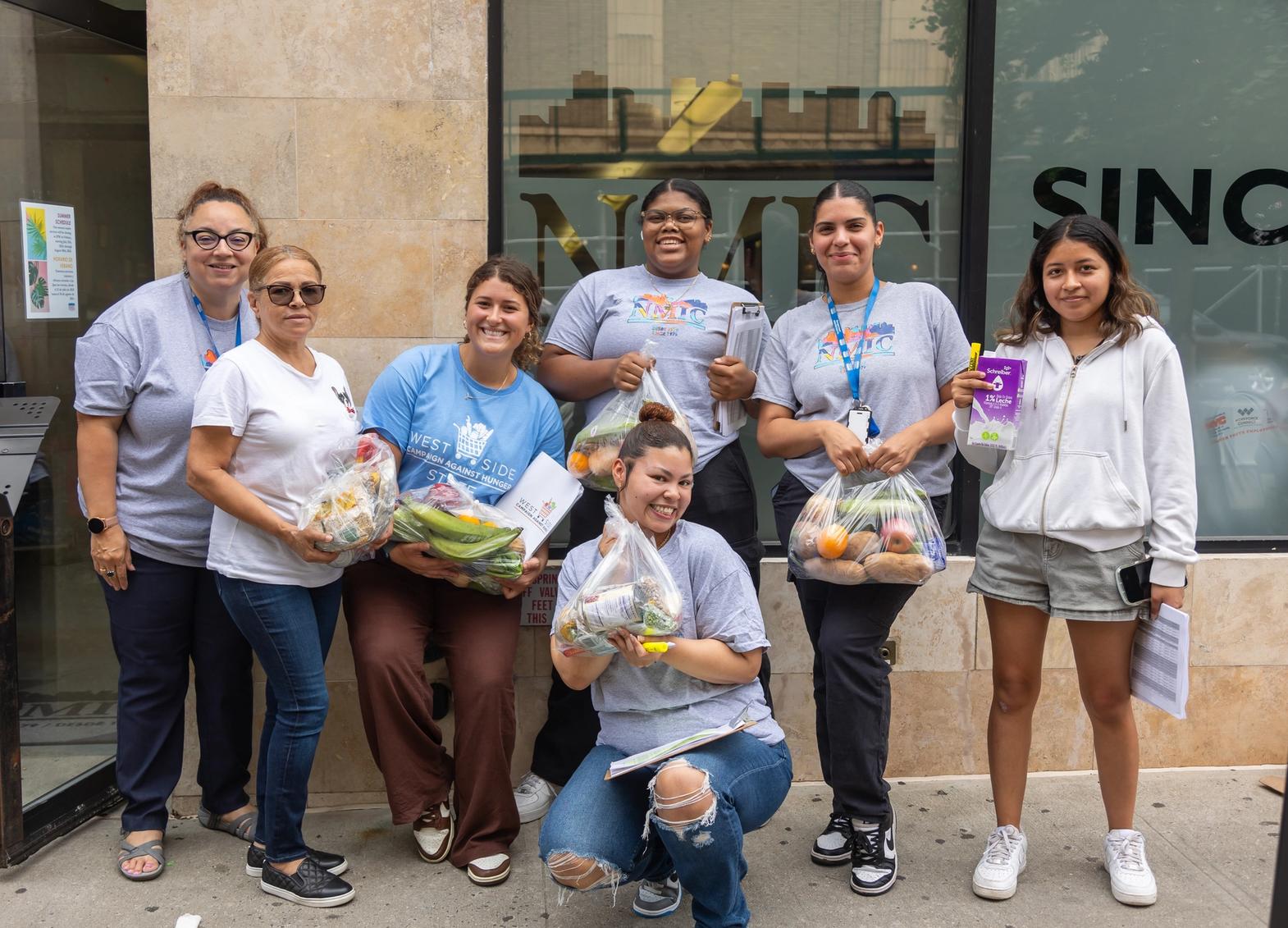 A line of WSCAH volunteers pose and smile, clutching bags of fresh produce.