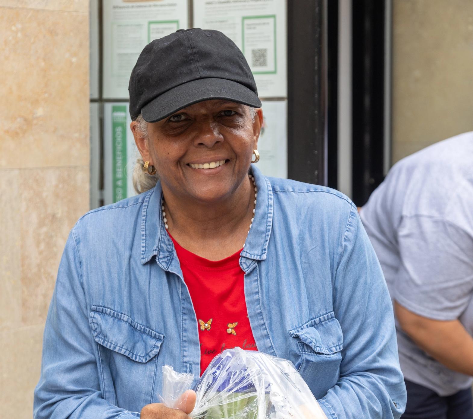 A woman smiles on a sunny day, holding a bag of produce she received from WSCAH.
