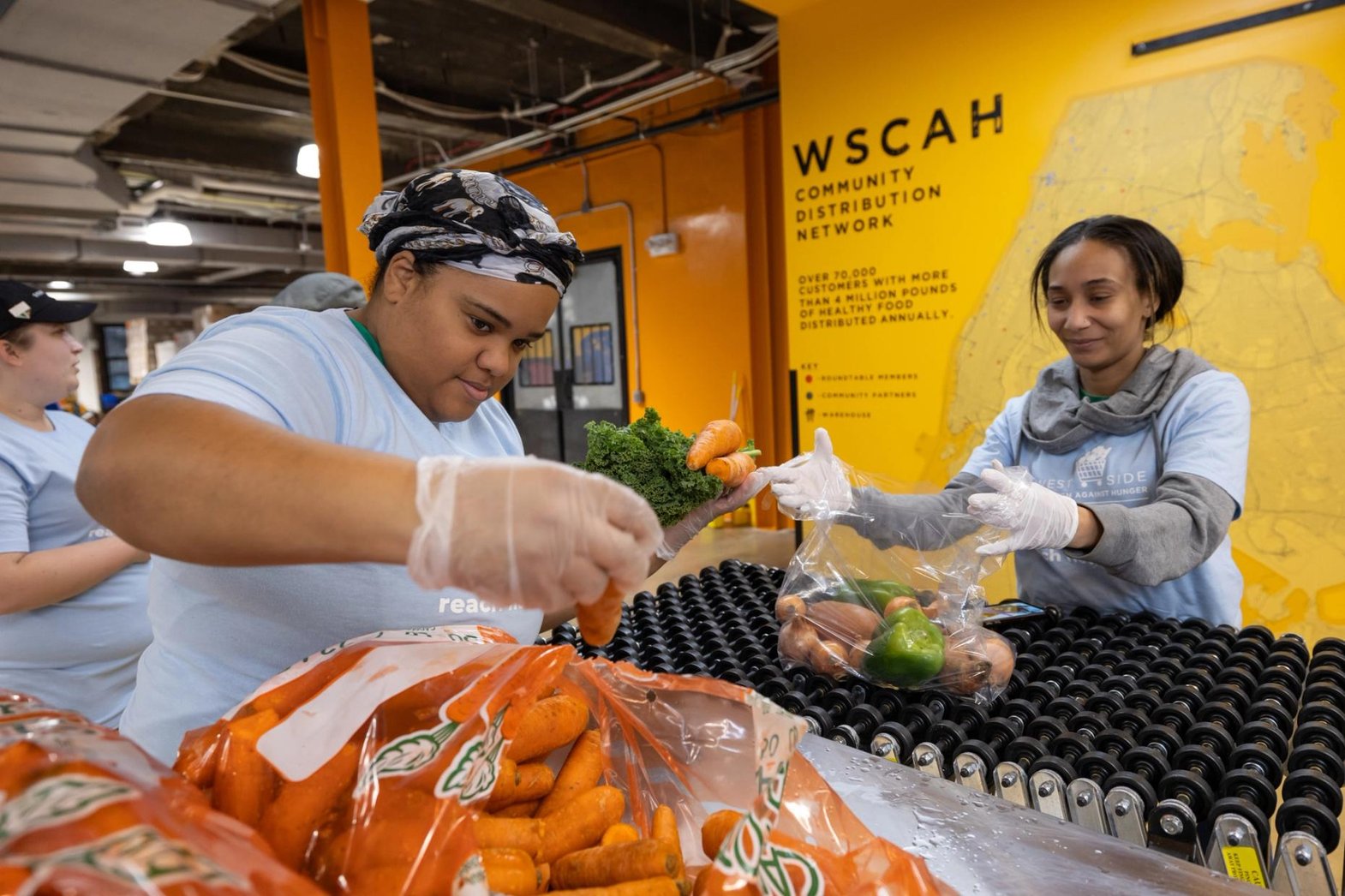 Two WSCAH volunteers are hard at work in our warehouse, packing carrots into a bag of fresh produce.