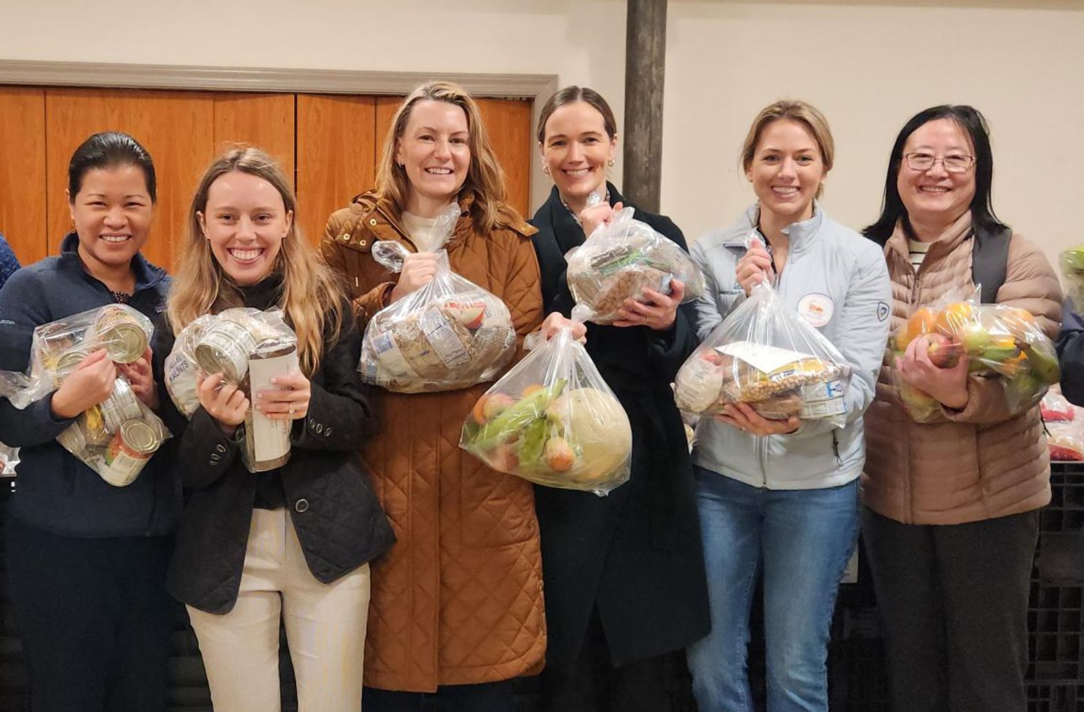 A group of six, smiling volunteers hold bags of fresh produce.
