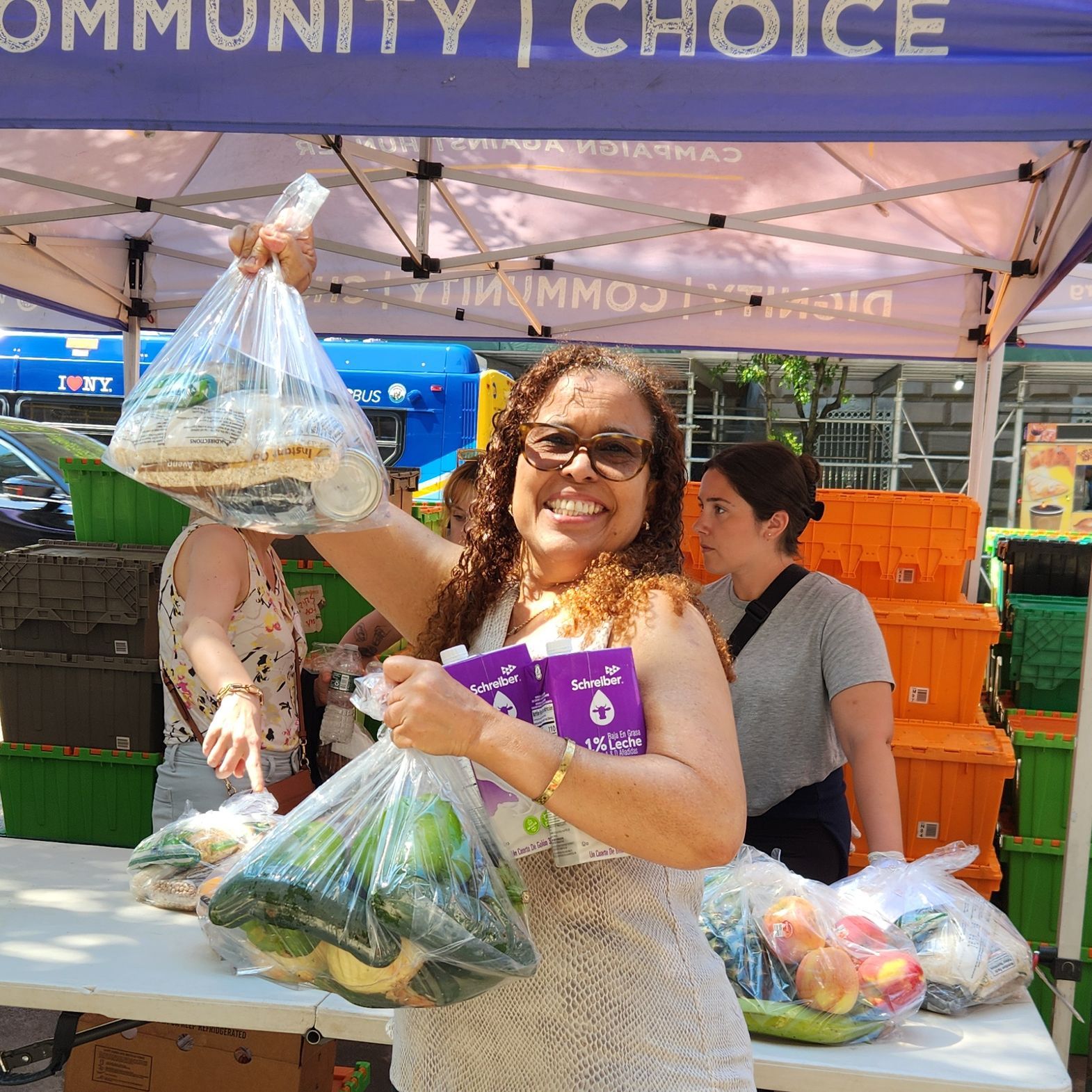 A woman wearing sunglasses stands in front of a WSCAH distribution with two bags of produce and two cartons of milk