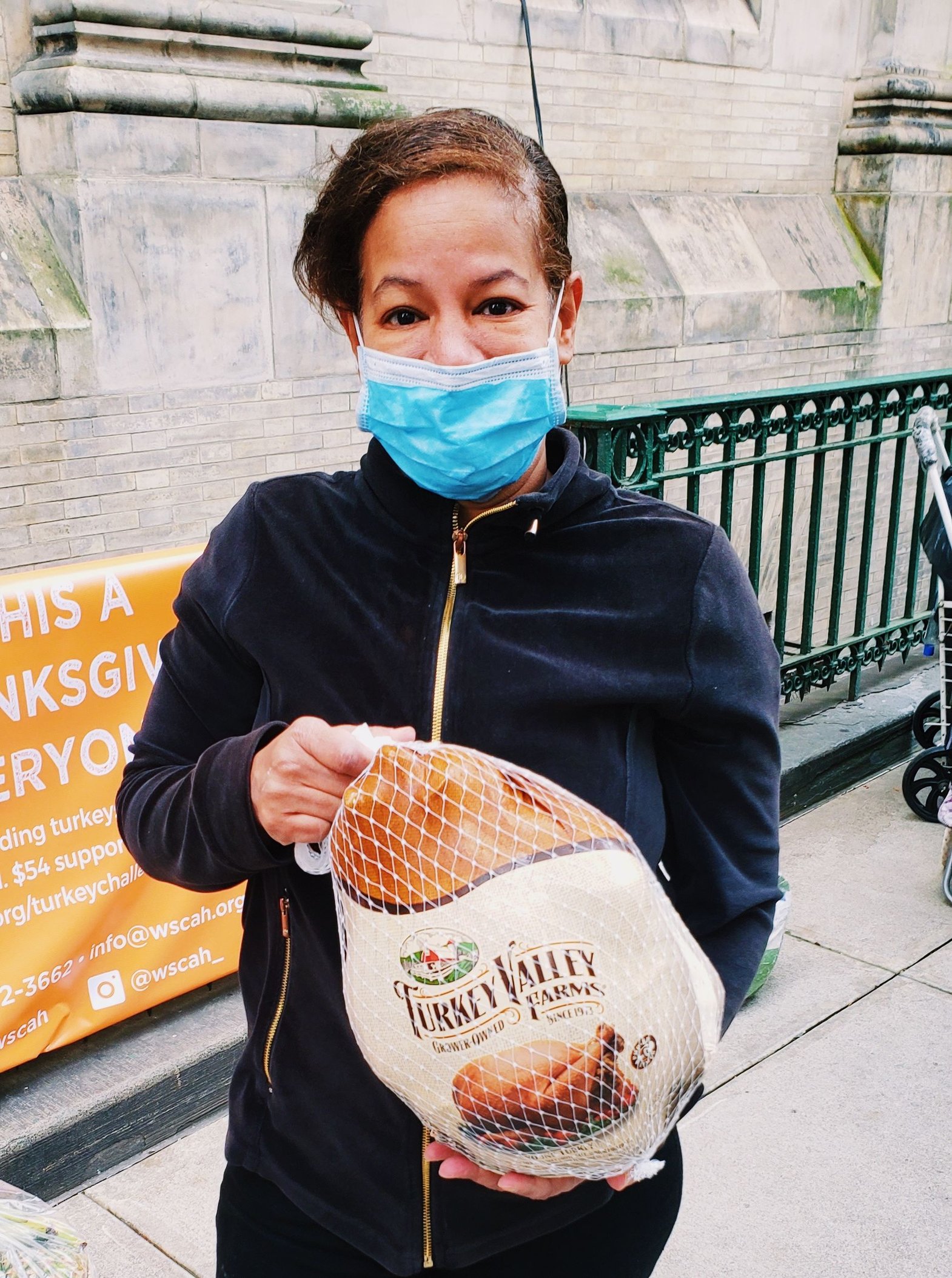 A customer wearing a facemask holds a turkey, taken on a sunny day outside of WSCAH's 86th street location