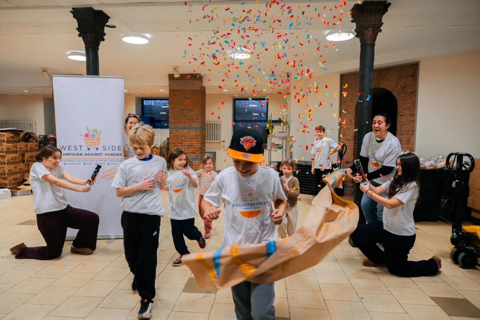 Kids run through a paper banner with confetti at volunteerfest